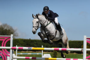 Grey horse Inlaws Manolo jmuping a fence with Derek McConnell on board