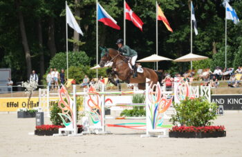 Niam McEvoy jumping a fence on her horse BP Rocket Man with flags flying in the background