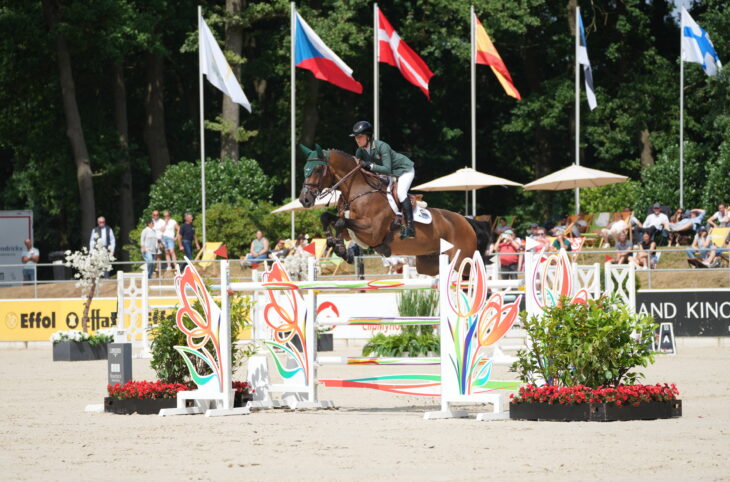 Niam McEvoy jumping a fence on her horse BP Rocket Man with flags flying in the background